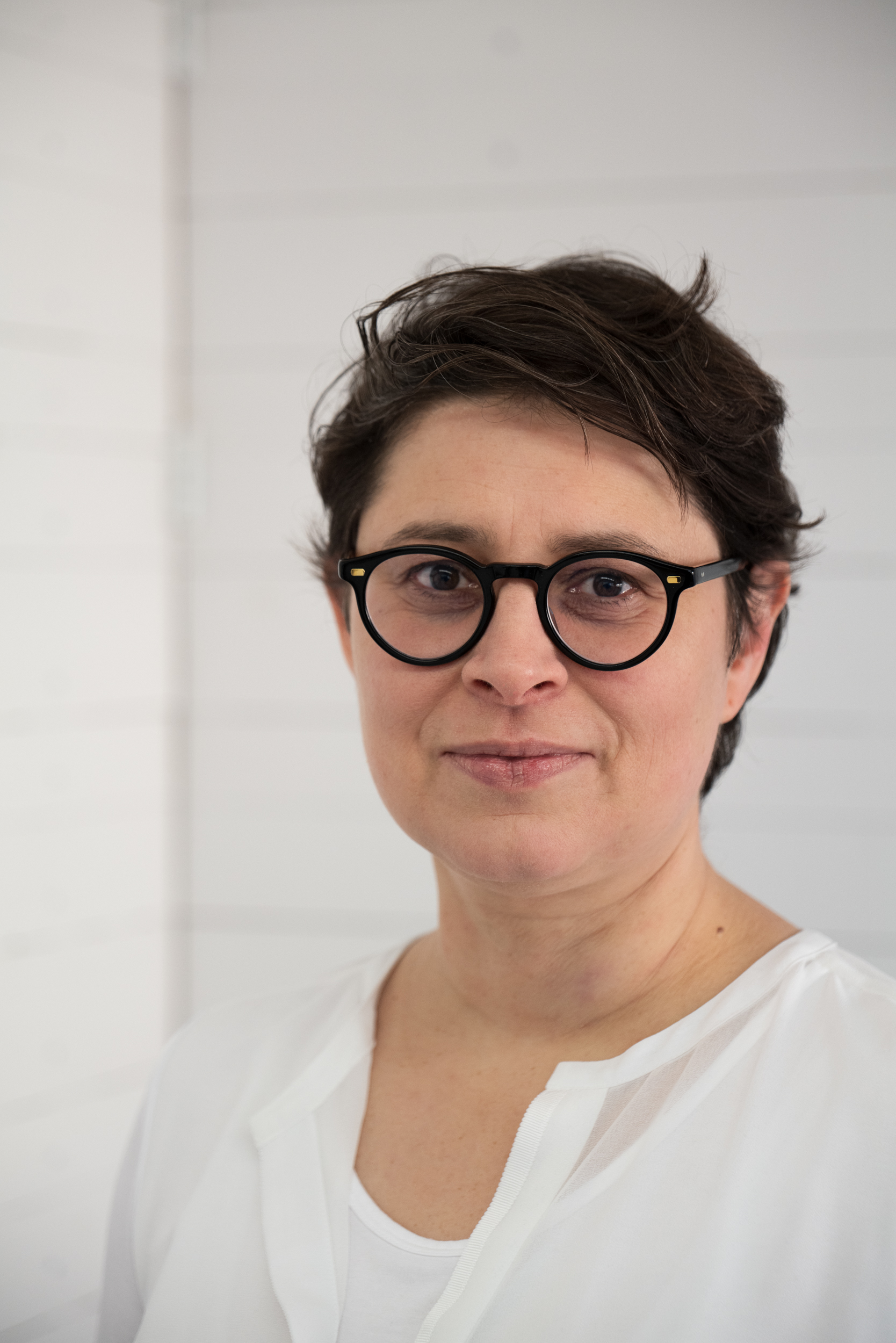 Mittelalte, kurzhaarige, dunkelhaarige Frau mit Brille, lächelnd.